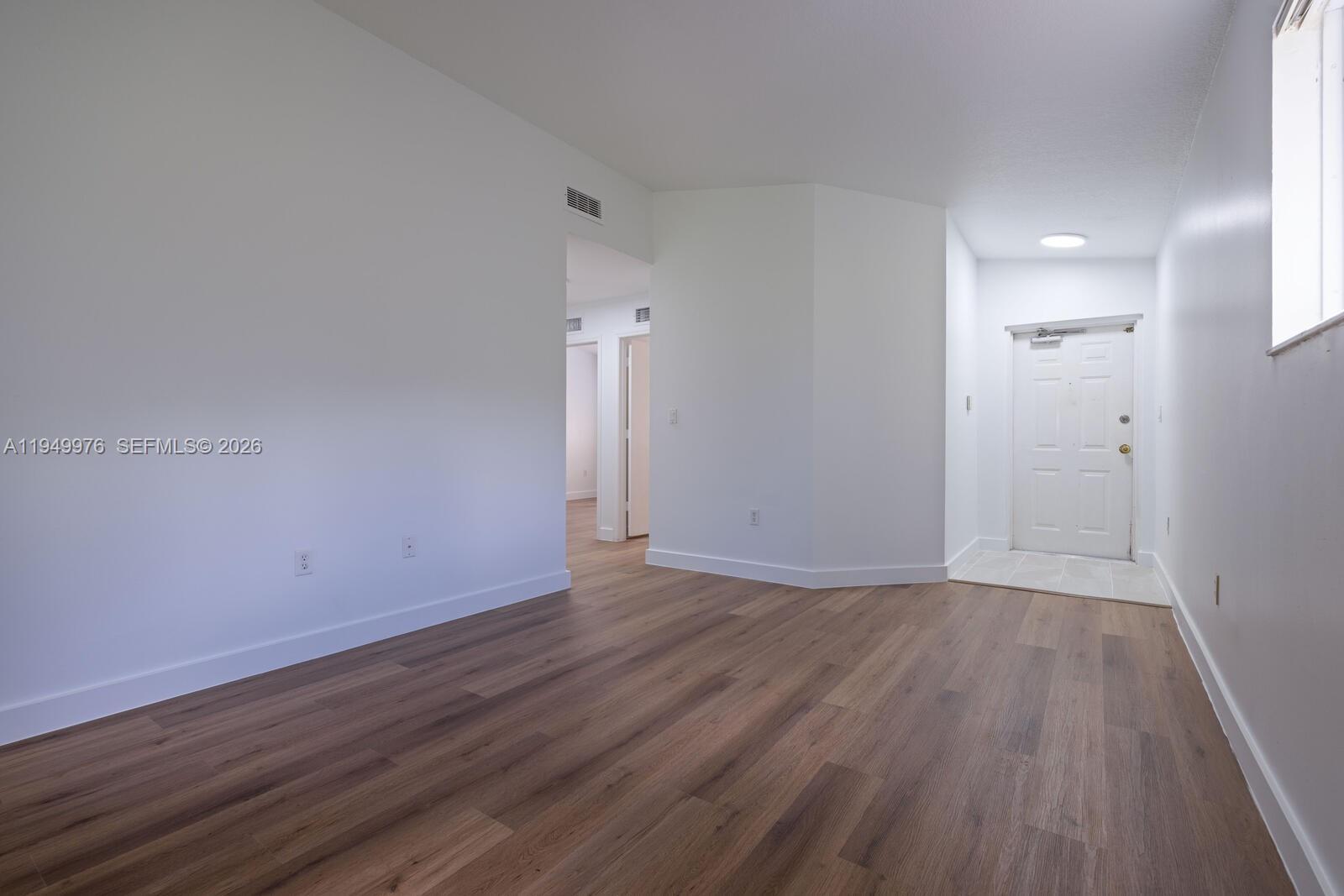 An empty room with white walls, wood-look flooring, and a white entry door — 990 NE 33rd Ter # 201, Homestead FL 33033, HOMESTEAD, FL