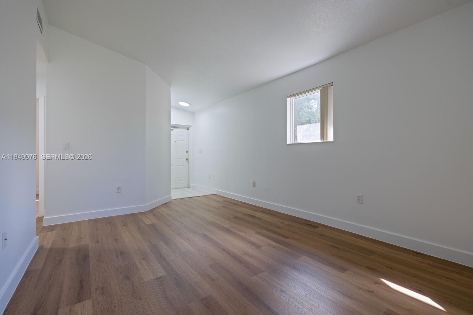 An empty room features white walls, light wood-look flooring, and a single window — 990 NE 33rd Ter # 201, Homestead FL 33033, HOMESTEAD, FL