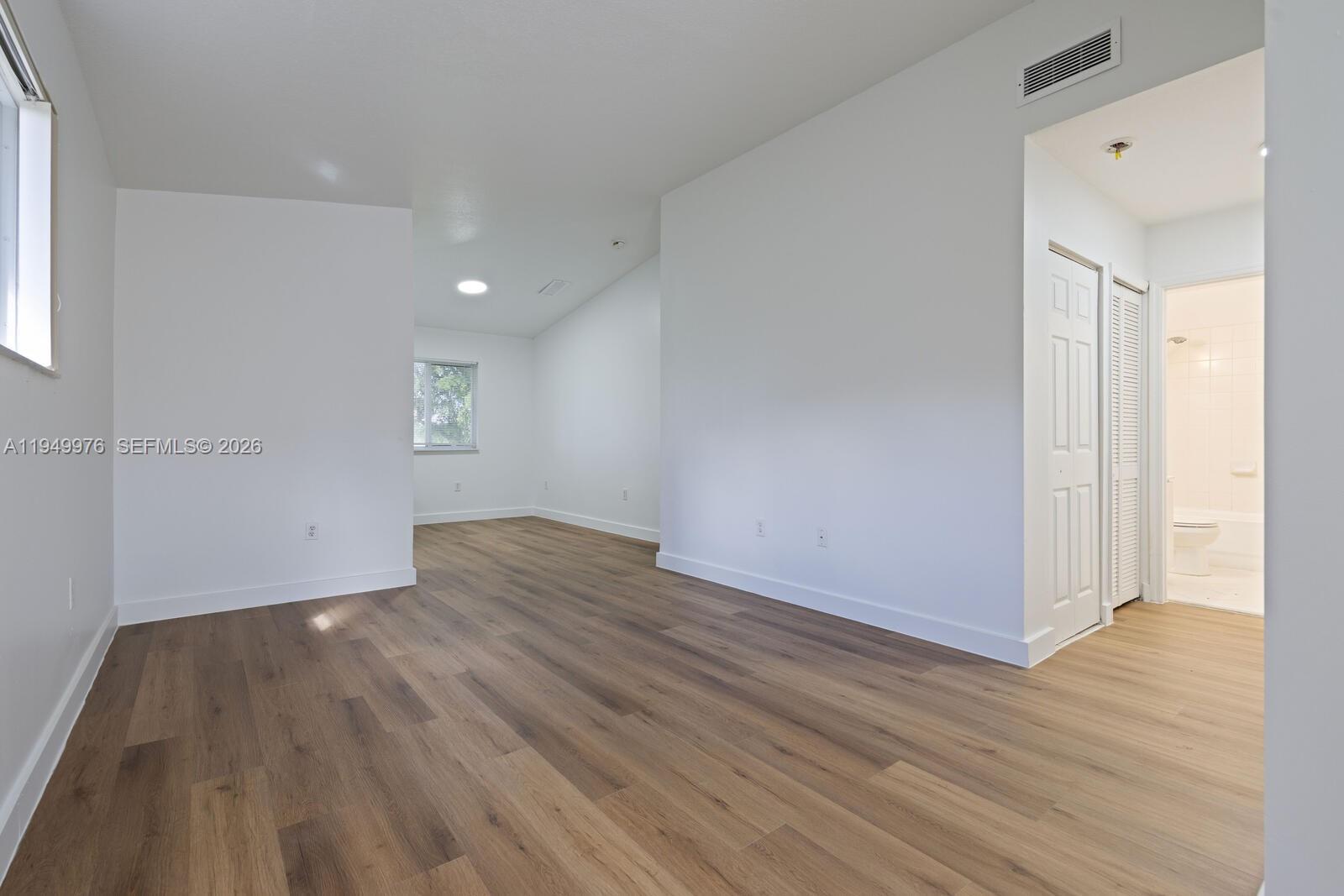 An empty room with white walls, wood-look flooring, and an attached bathroom with a tub — 990 NE 33rd Ter # 201, Homestead FL 33033, HOMESTEAD, FL