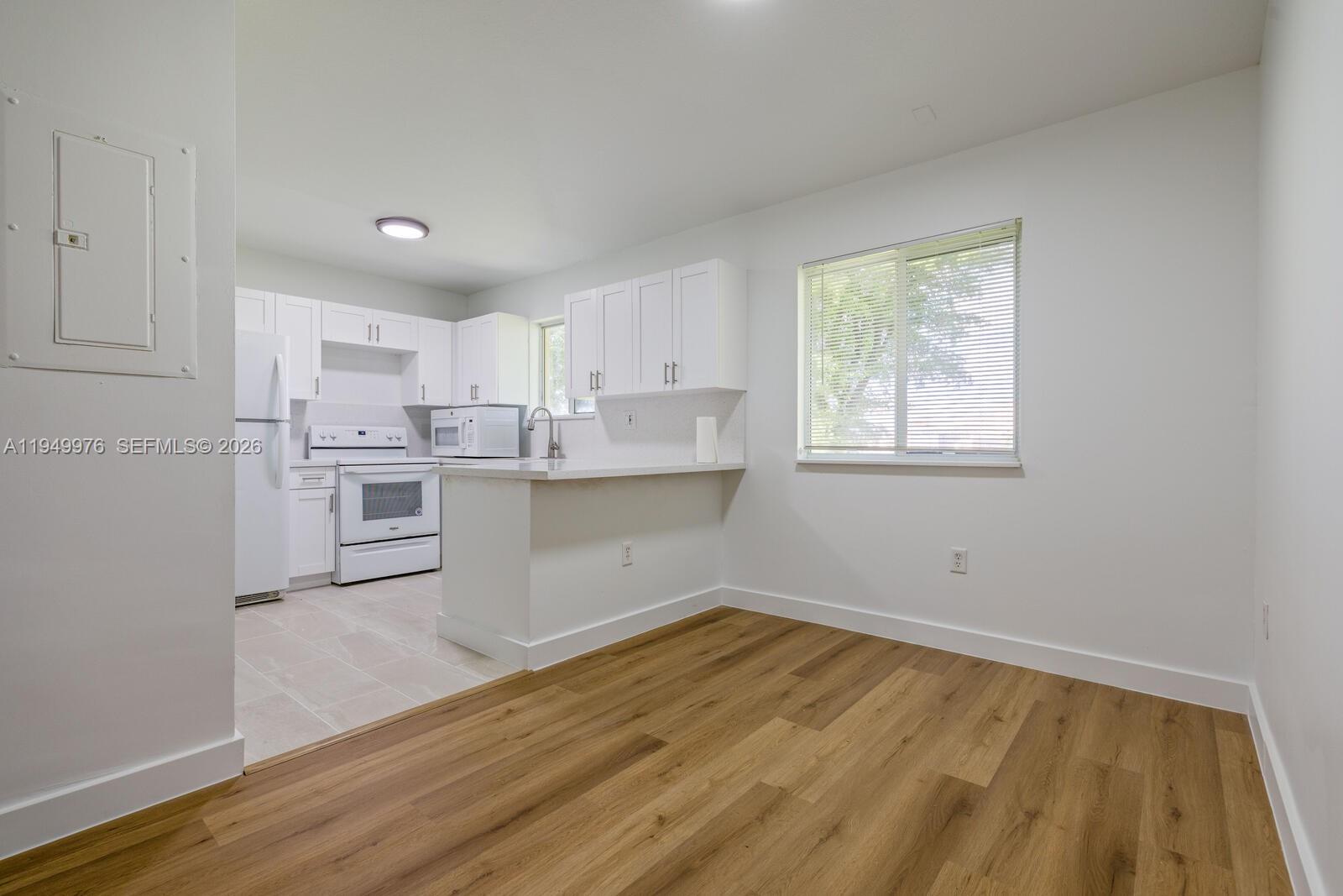 A kitchen with white cabinets and appliances opens into a room with wood flooring — 990 NE 33rd Ter # 201, Homestead FL 33033, HOMESTEAD, FL