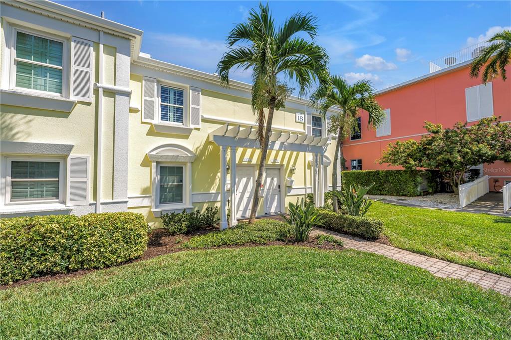 A yellow two-story townhouse exterior features a white pergola entrance and a palm tree — 4982 COQUINA KEY DRIVE SE, ST PETERSBURG, FL