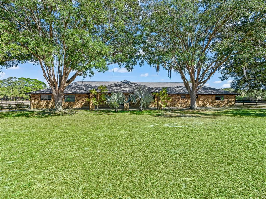 A single-story brick house with a covered porch sits behind a large, mowed grassy lawn — 9865 SW 74TH AVENUE, OCALA, FL
