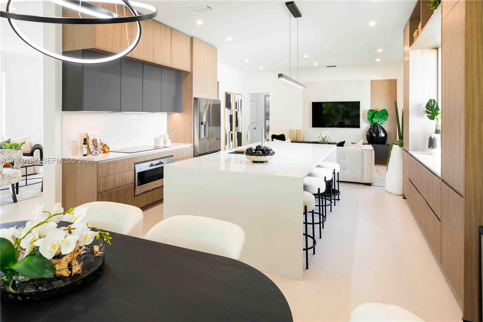 A modern kitchen features a large white island, wood cabinetry, and an adjacent dining area — 16012 Opal Creek Dr, Weston FL 33331, WESTON, FL