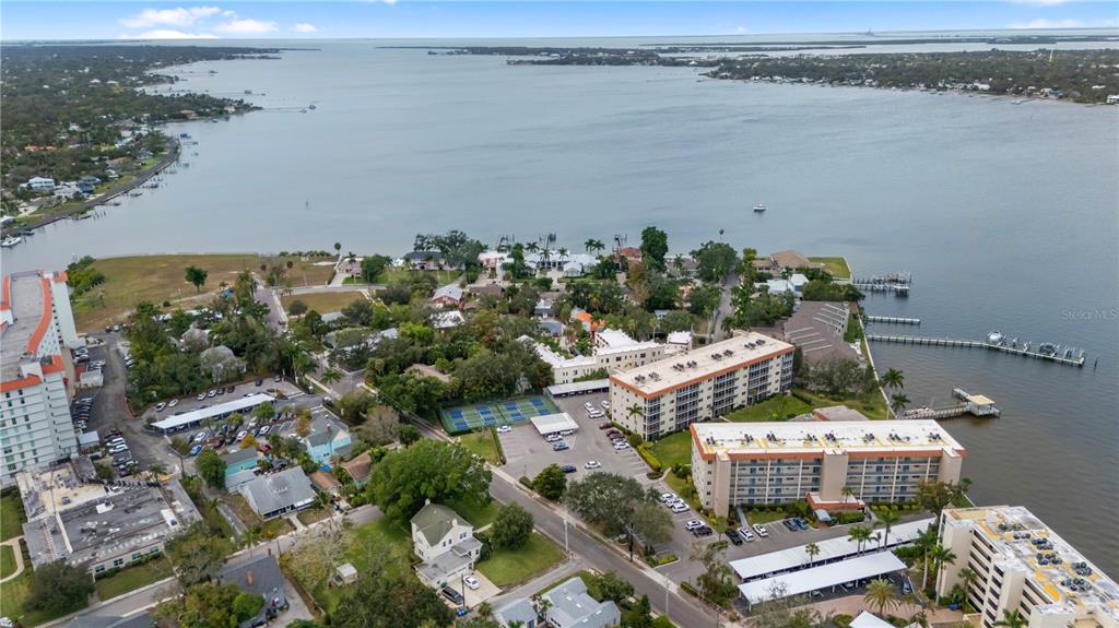 An aerial view shows waterfront apartment buildings, a parking lot, tennis courts, and boat docks — 1650 1ST AVENUE W UNIT 307B, BRADENTON, FL