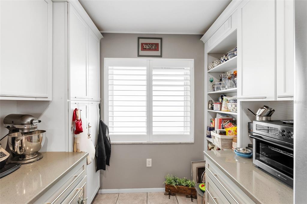 A kitchen nook features white cabinetry, quartz countertops, open shelving, and a window with shutters — 1650 1ST AVENUE W UNIT 307B, BRADENTON, FL
