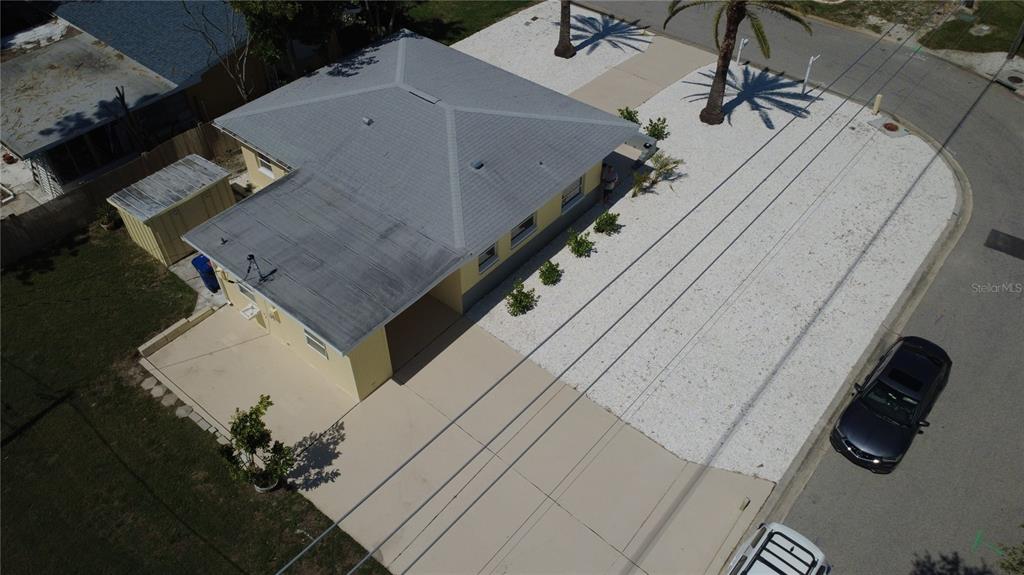 An aerial view shows a yellow house with a gray roof, concrete driveway, and gravel yard — 1404 COREY WAY S, SOUTH PASADENA, FL