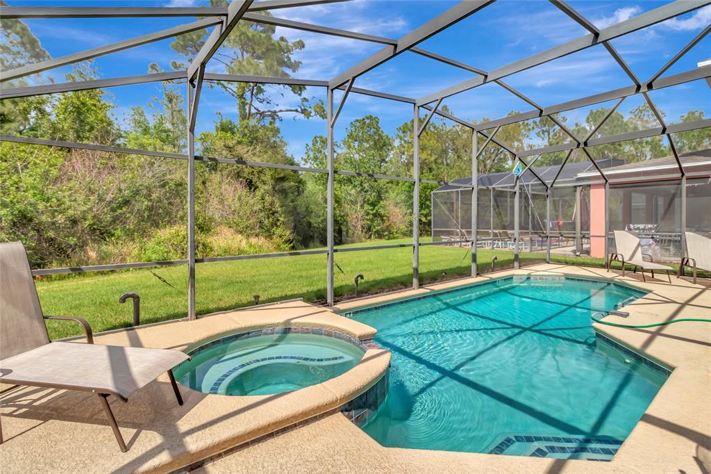 A screened-in pool and spa area with lounge chairs overlooking a grassy backyard — 4703 GOLDEN BEACH COURT, KISSIMMEE, FL