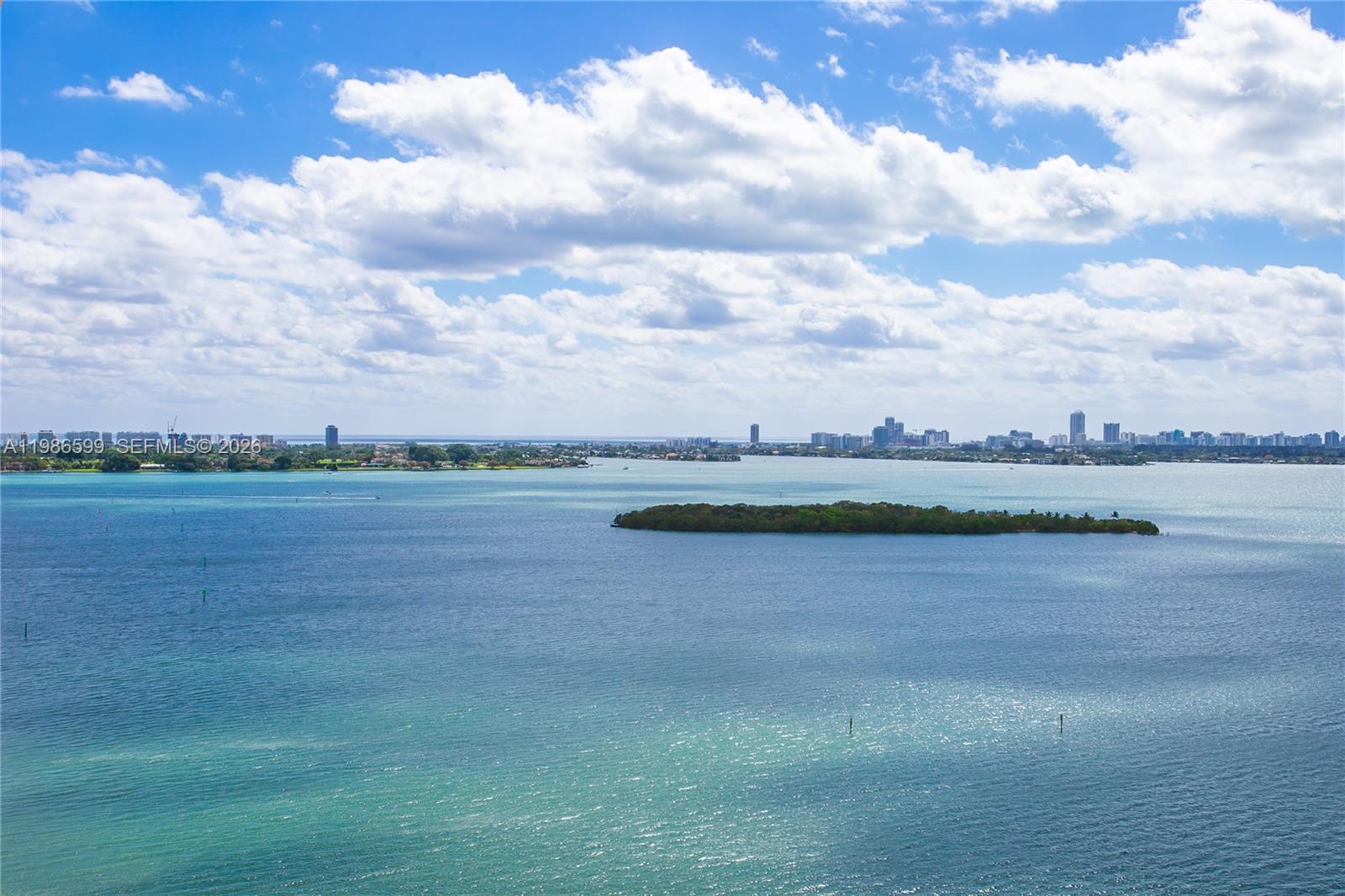 An aerial view shows a small island surrounded by blue water with a distant city skyline — 1800 NE 114th St # 2309, Miami FL 33181, MIAMI, FL