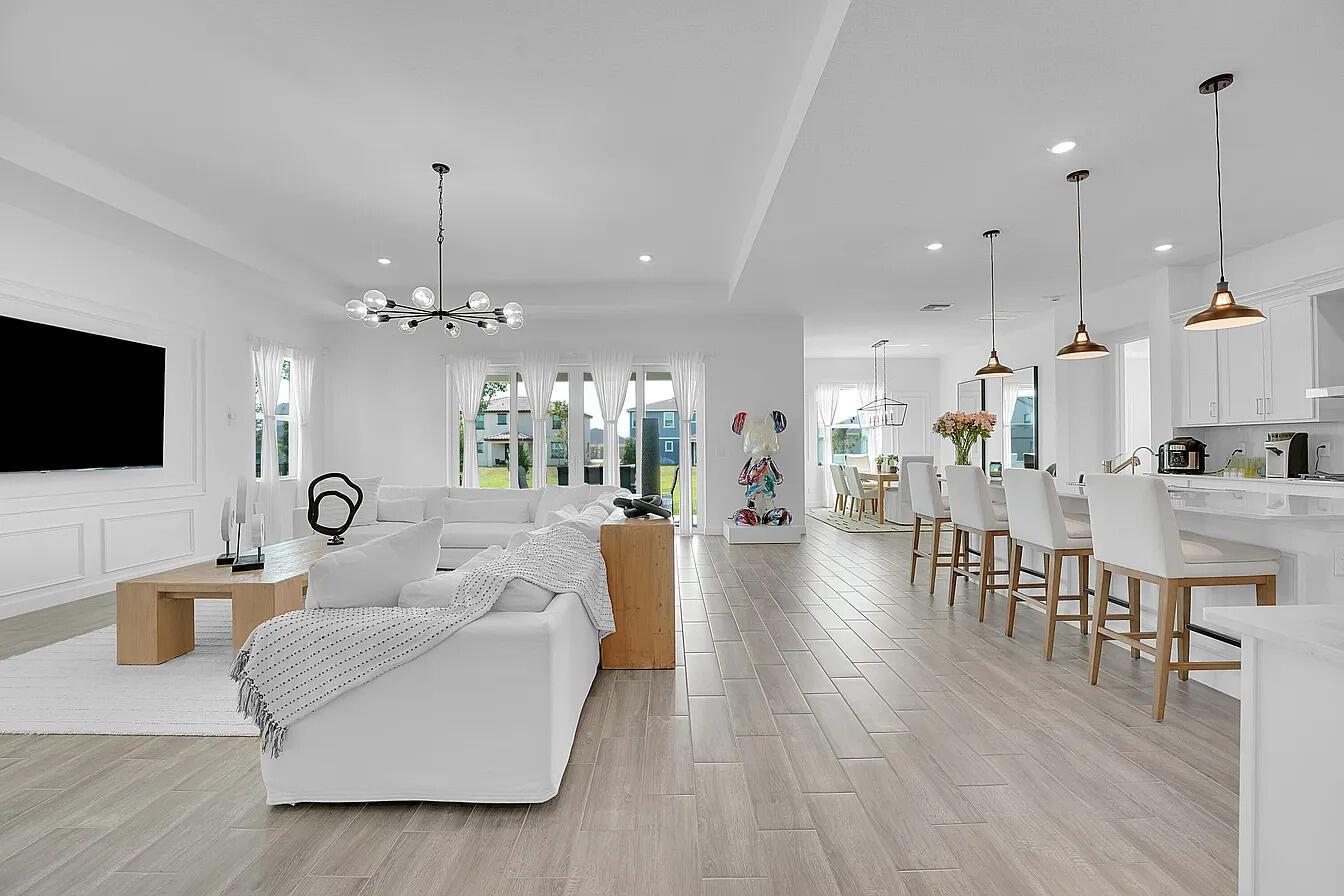 An open-concept living room and kitchen featuring white furniture, light wood accents, and tile flooring — 1113 Tangled Orchard Trace, FL 33470, FL