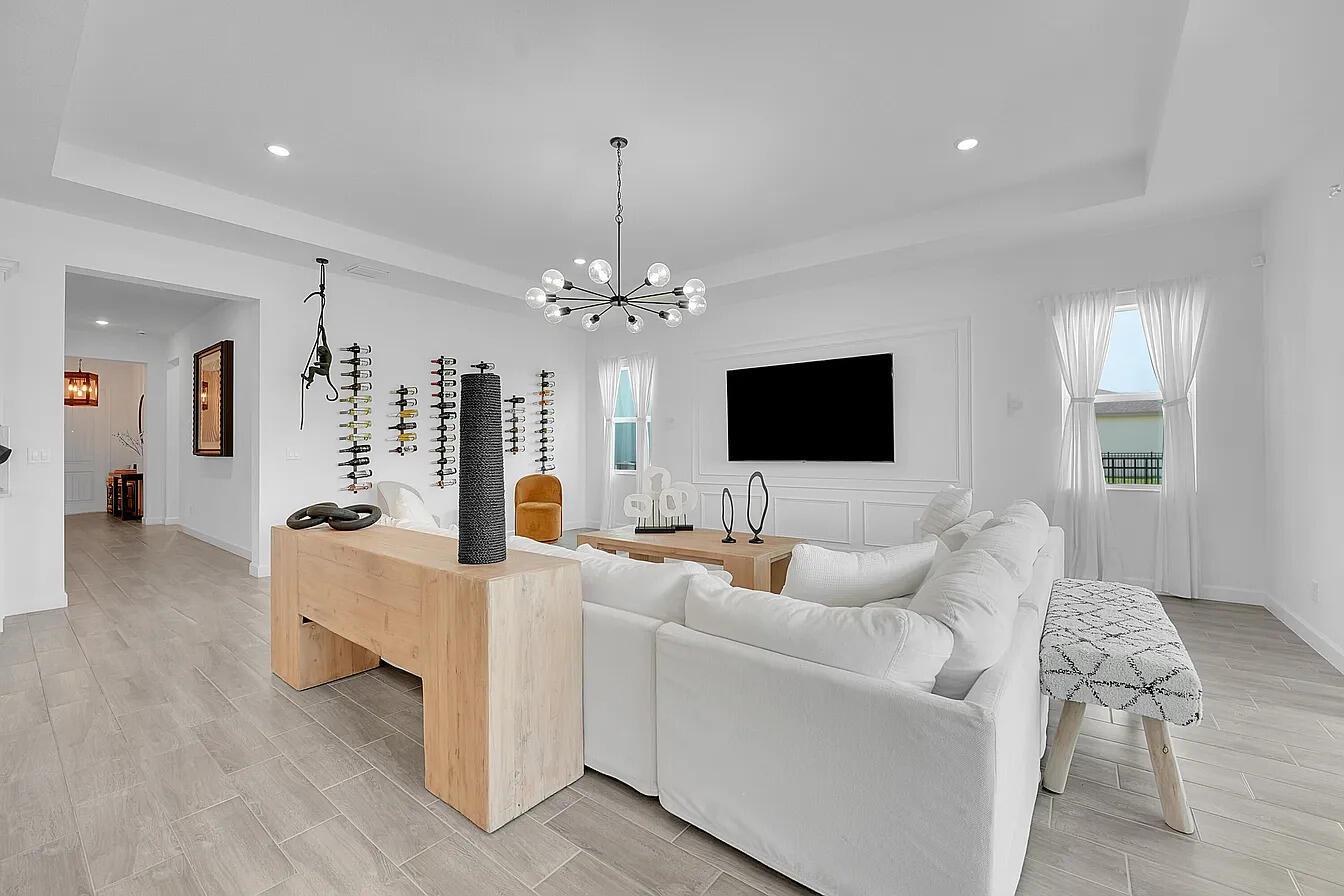 A bright living room features a white sectional sofa, a wooden console table, and a chandelier — 1113 Tangled Orchard Trace, FL 33470, FL
