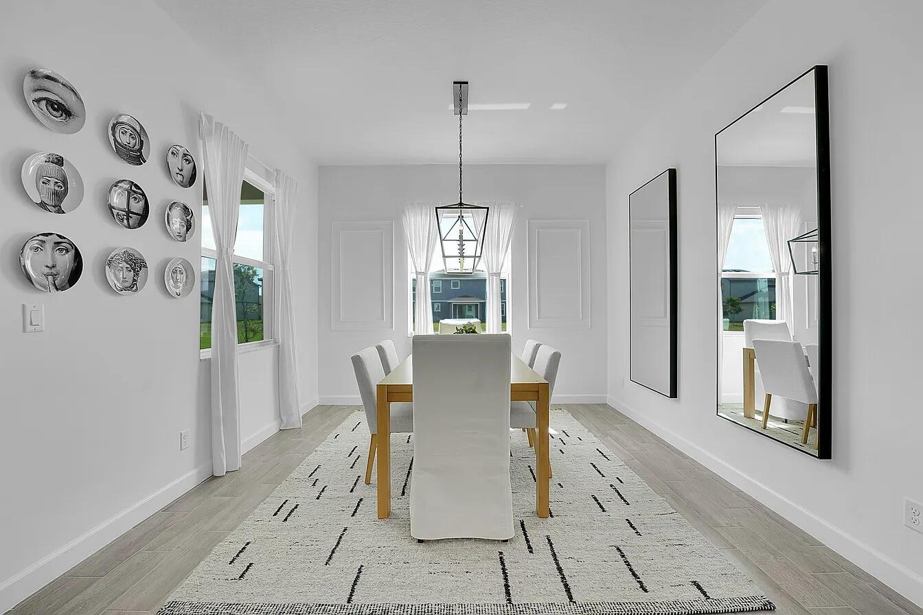 A dining room features a wooden table, white chairs, a patterned rug, and wall art — 1113 Tangled Orchard Trace, FL 33470, FL