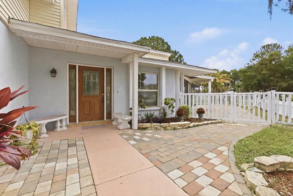 A paved walkway leads to the front entrance of a house with a wooden door — 3235 SILKWOOD LOOP, LAND O LAKES, FL