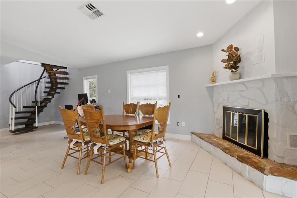 A dining area features a wooden table, chairs, a stone fireplace, and a spiral staircase — 3235 SILKWOOD LOOP, LAND O LAKES, FL