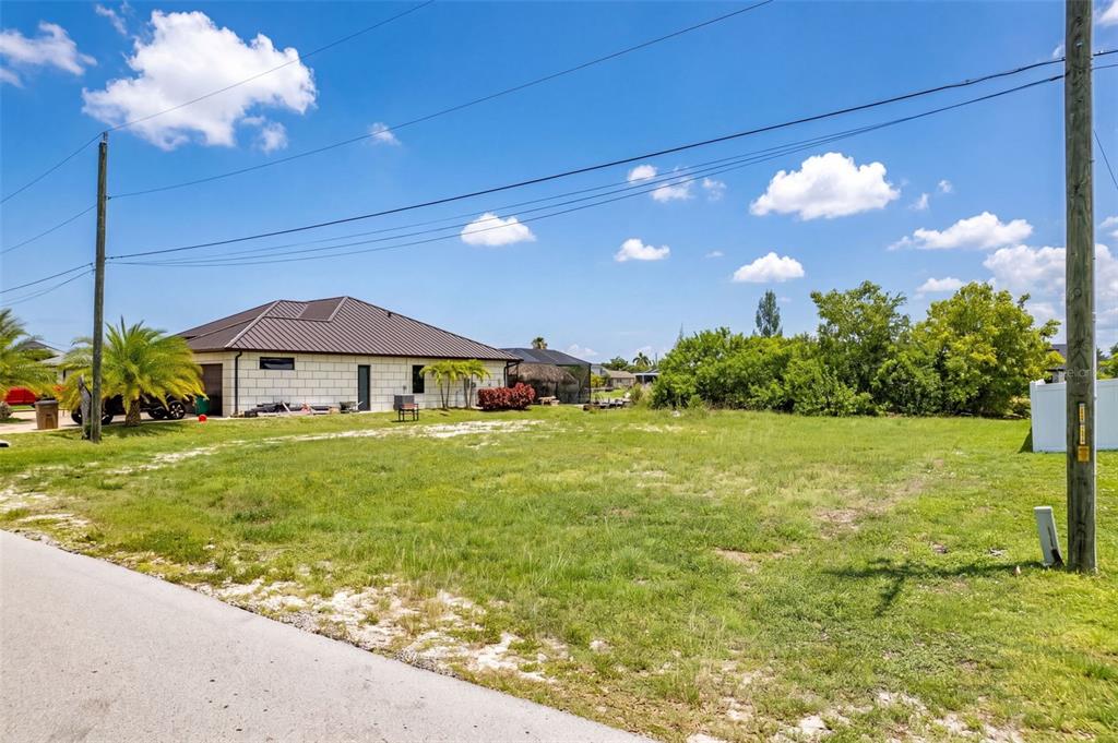 A vacant grassy lot sits next to a single-story house with a metal roof — 623 NE 7TH TERRACE, CAPE CORAL, FL
