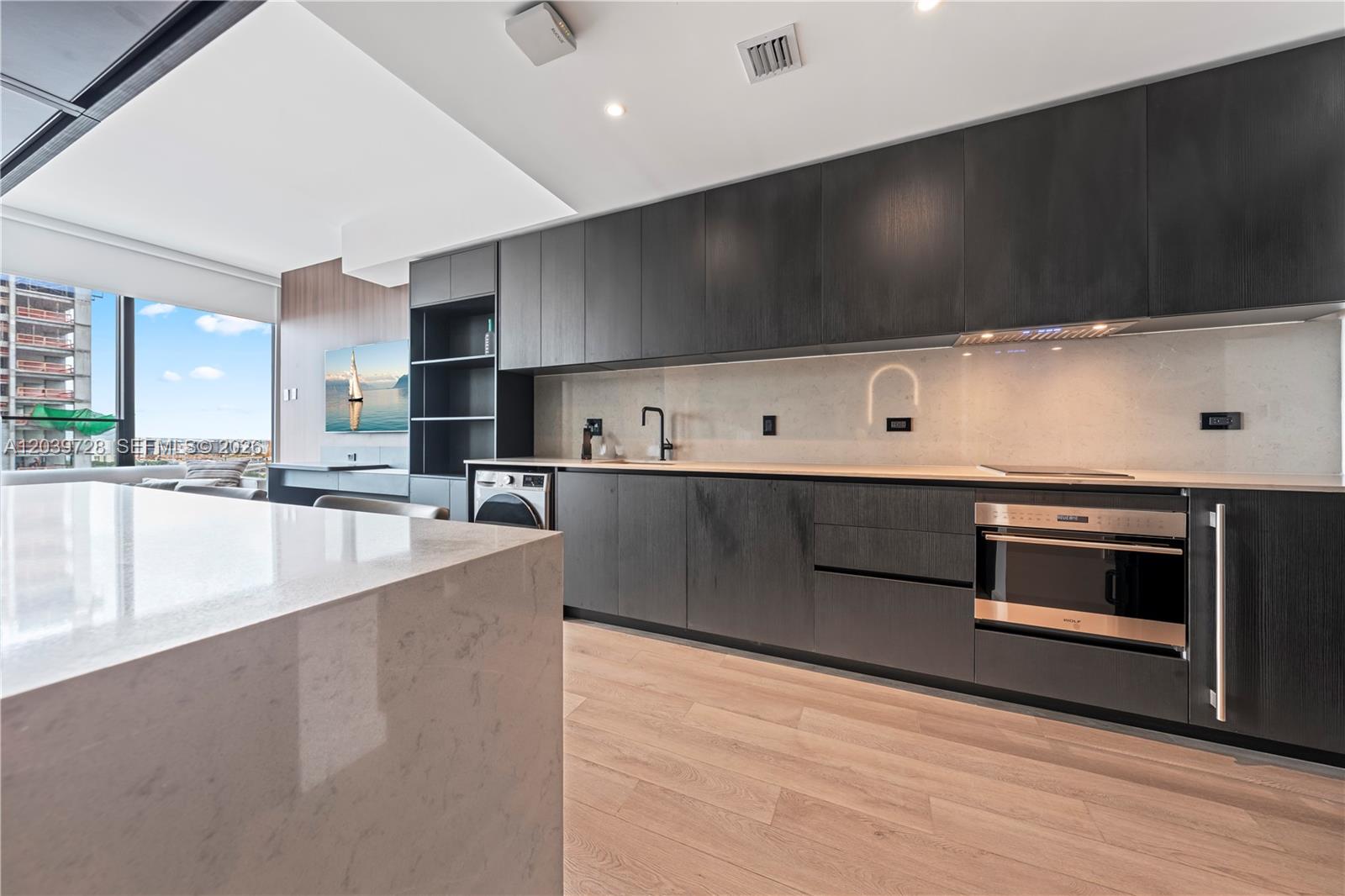 A modern kitchen features dark wood cabinetry, a stone island, and a built-in oven — 20 NE 11th St # 2211, Miami FL 33132, MIAMI, FL