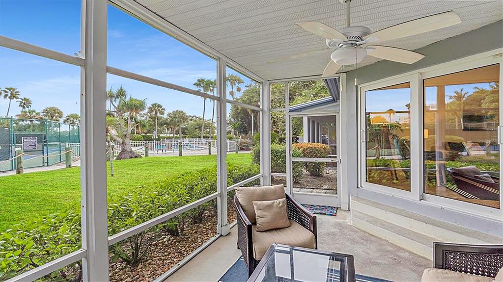 A screened-in patio features a ceiling fan, wicker furniture, and a view of a tennis court — 1204 SIESTA BAYSIDE DRIVE UNIT 1204-D, SARASOTA, FL