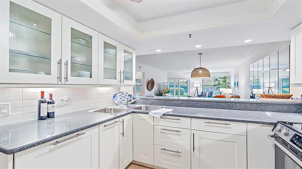 A white kitchen features gray granite countertops, glass-front upper cabinets, and an open-concept layout — 1204 SIESTA BAYSIDE DRIVE UNIT 1204-D, SARASOTA, FL