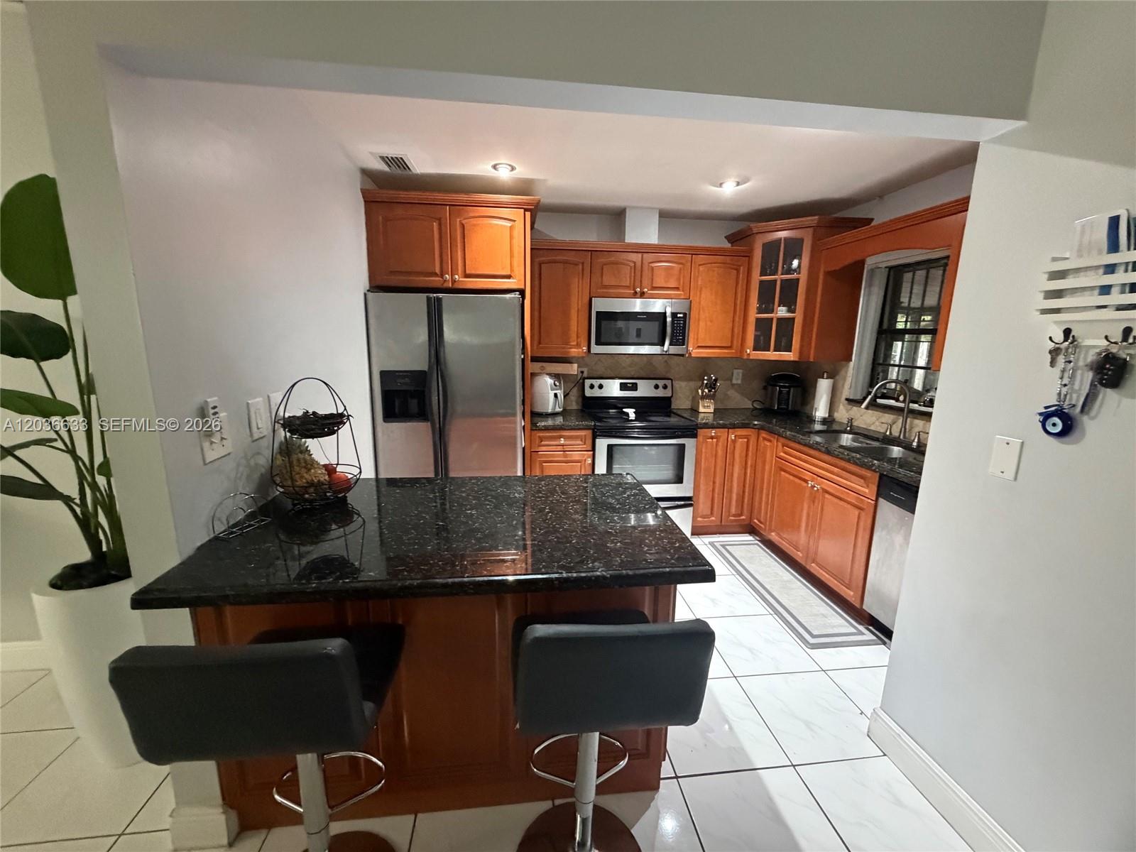 A kitchen features wood cabinets, black granite countertops, stainless steel appliances, and a breakfast bar — 5801 SW 144th Cir Pl # 5801, Miami FL 33183, MIAMI, FL