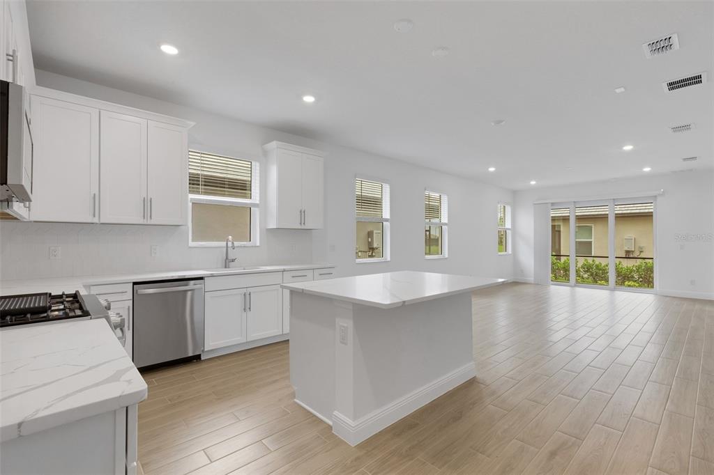 A modern kitchen features white cabinets, a central island, and light wood-look tile flooring — 18135 CHERISHED LOOP, BRADENTON, FL