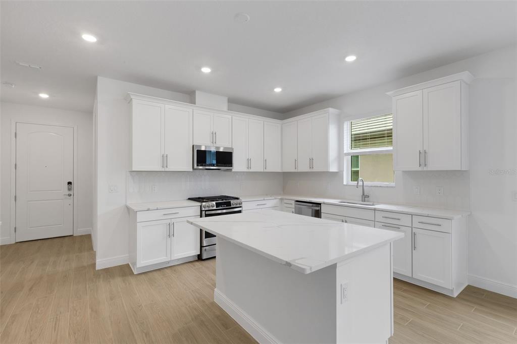 A modern kitchen features white cabinets, a marble-topped island, and light wood-look flooring — 18135 CHERISHED LOOP, BRADENTON, FL