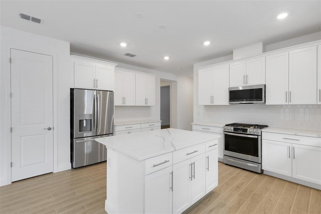 A modern kitchen features white cabinetry, a marble-topped island, stainless steel appliances, and wood-look flooring — 18135 CHERISHED LOOP, BRADENTON, FL
