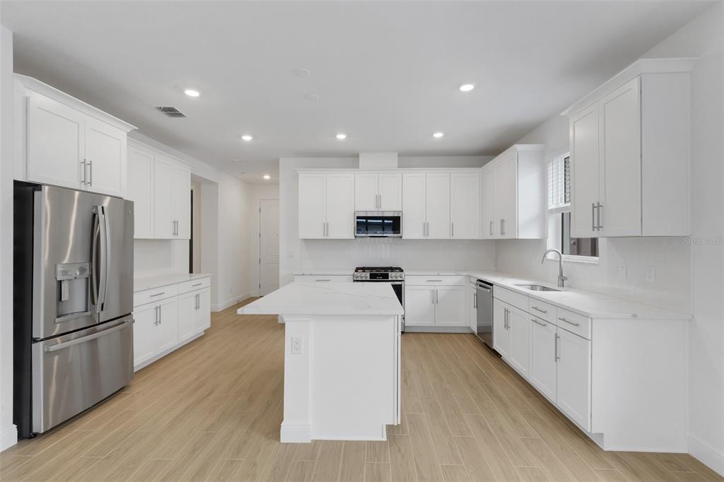 A modern kitchen features white cabinetry, stainless steel appliances, a center island, and light flooring — 18135 CHERISHED LOOP, BRADENTON, FL