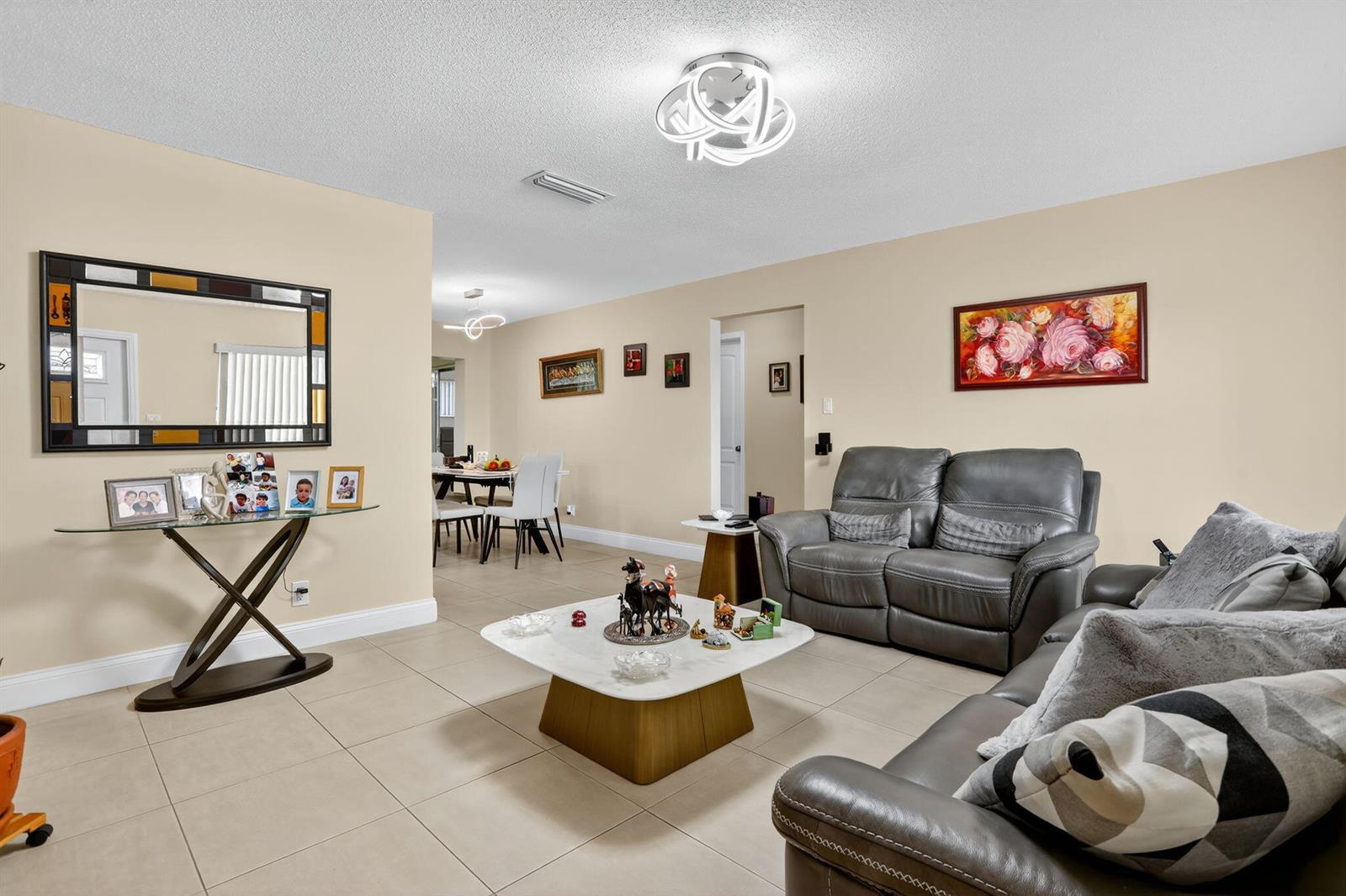 A living room with beige walls, tile flooring, gray leather furniture, and a modern light fixture — 6945 NW 14th Street, Margate FL 33063, MARGATE, FL