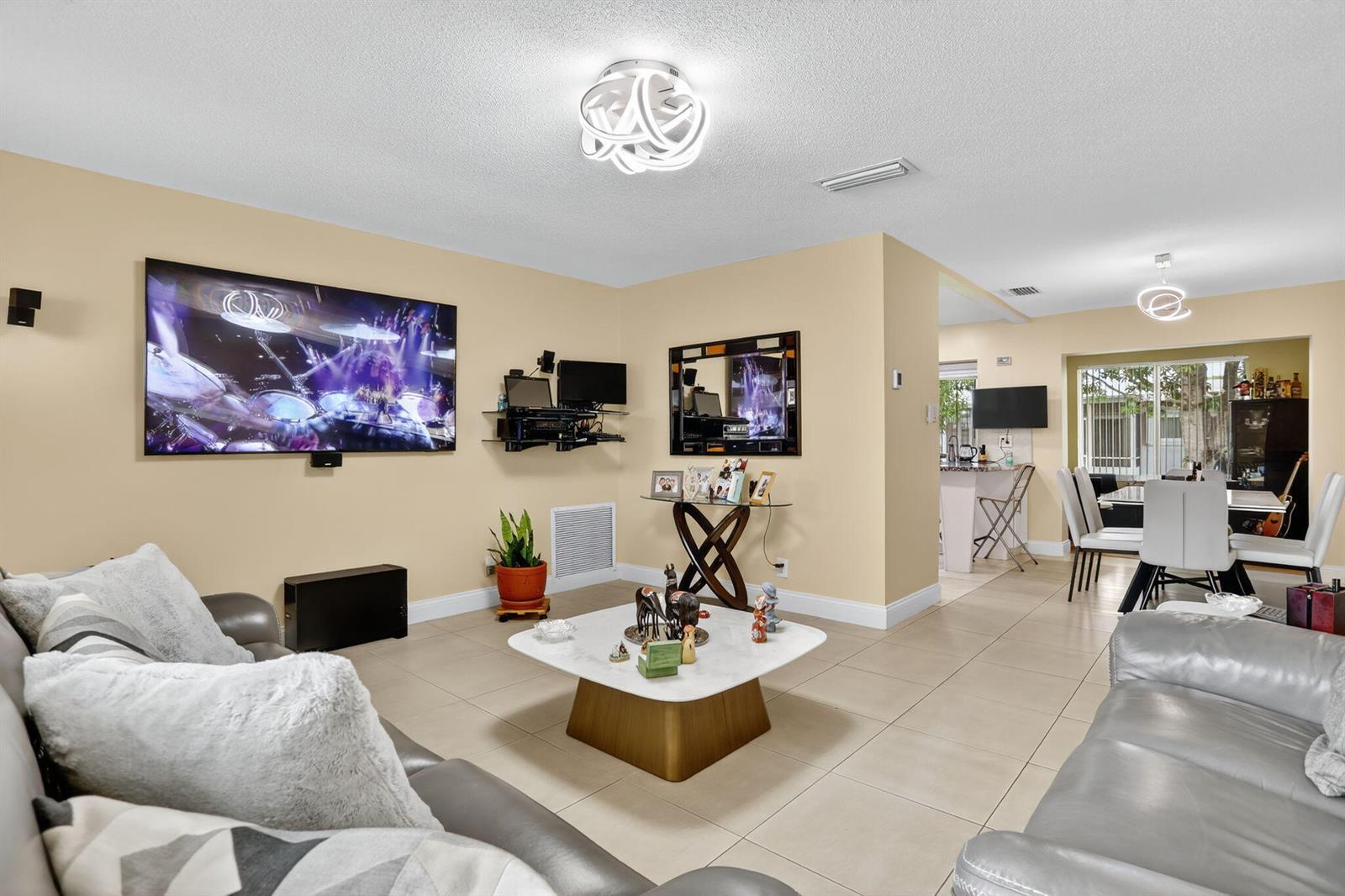 A living room features light tile floors, a large wall-mounted television, and a central coffee table — 6945 NW 14th Street, Margate FL 33063, MARGATE, FL