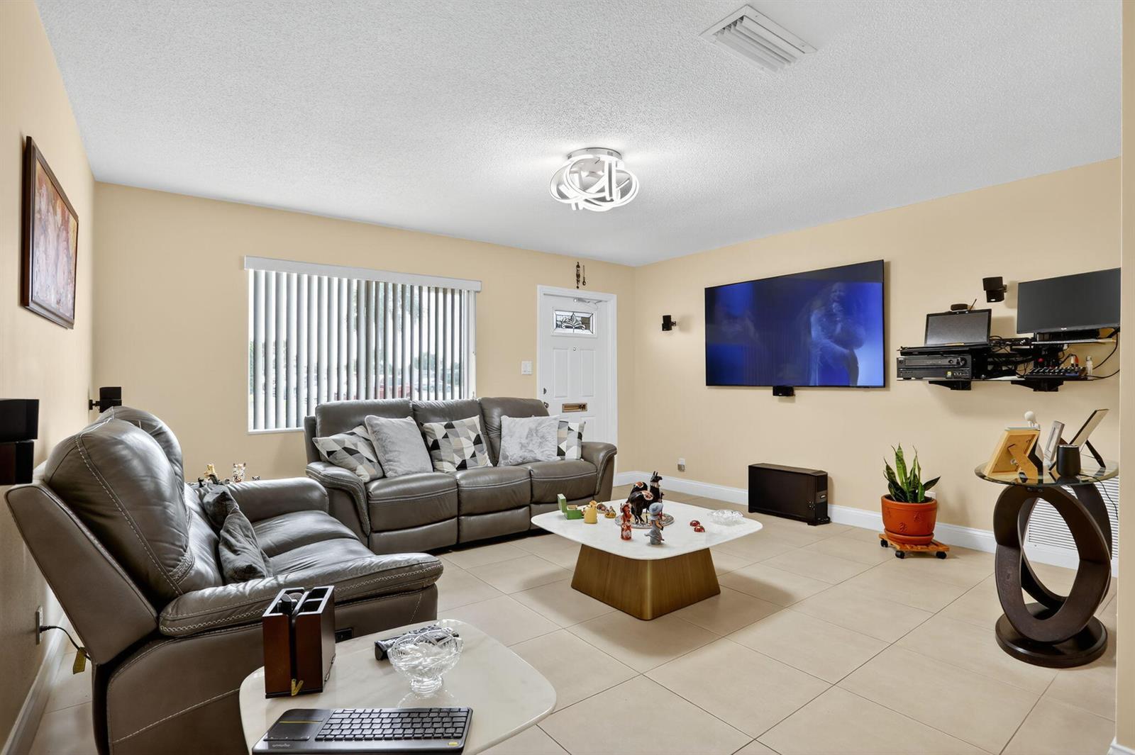 A living room features light tile flooring, beige walls, grey leather sofas, and a wall-mounted television — 6945 NW 14th Street, Margate FL 33063, MARGATE, FL
