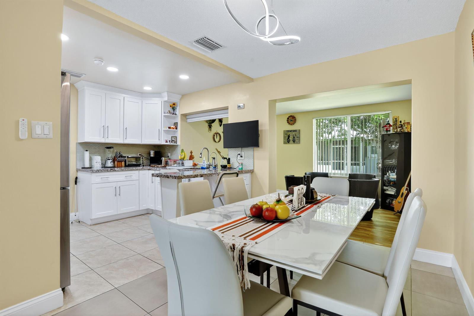 A dining area with a marble-top table sits adjacent to a white kitchen with granite countertops — 6945 NW 14th Street, Margate FL 33063, MARGATE, FL
