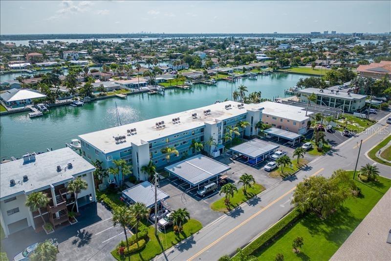 An aerial view shows a multi-story apartment building with covered parking and a waterfront location — 12405 3RD STREET E UNIT 201, TREASURE ISLAND, FL