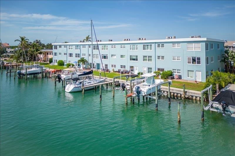 An aerial view of a light blue apartment building with boat slips along the water — 12405 3RD STREET E UNIT 201, TREASURE ISLAND, FL