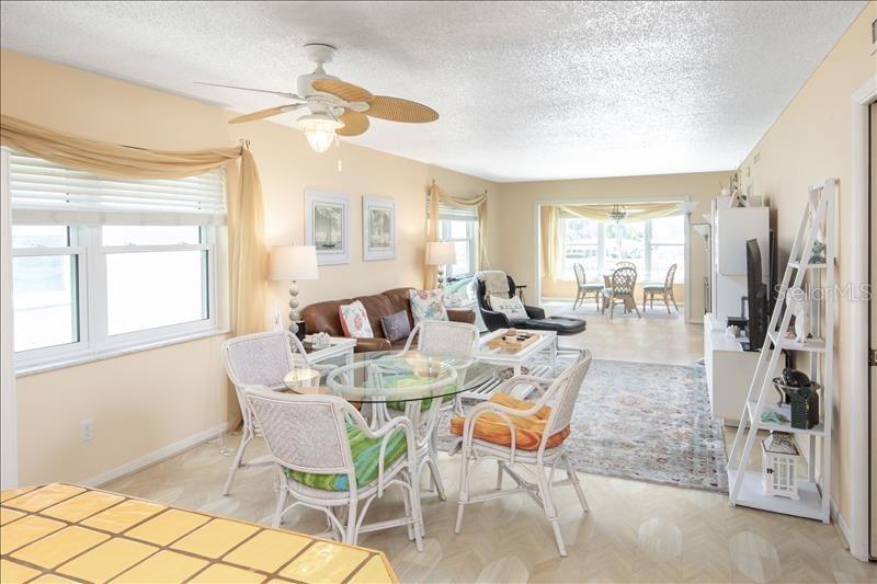 A living and dining area features wicker furniture, a glass table, and a ceiling fan — 12405 3RD STREET E UNIT 201, TREASURE ISLAND, FL