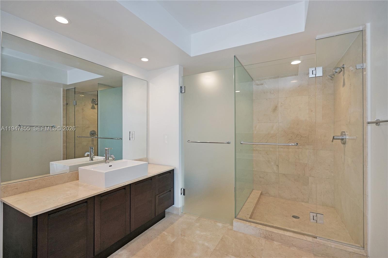 A modern bathroom features a dark wood vanity, vessel sink, and a glass-enclosed shower — SUNNY ISLES BEACH, FL