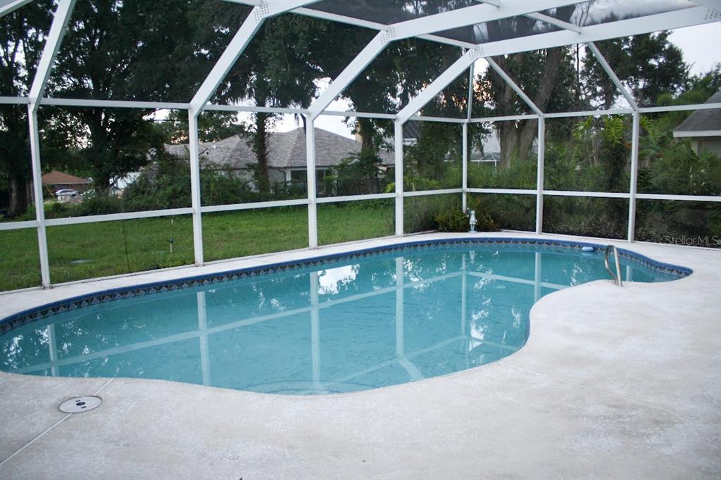 A swimming pool with a blue tile border is enclosed by a white screen cage — 1033 GLENHAM DRIVE NE, PALM BAY, FL