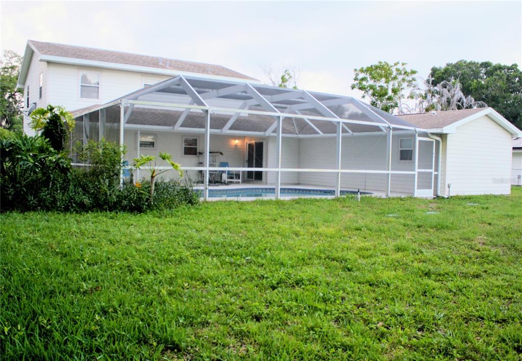 A swimming pool with a screened enclosure sits beside a white house — 1033 GLENHAM DRIVE NE, PALM BAY, FL