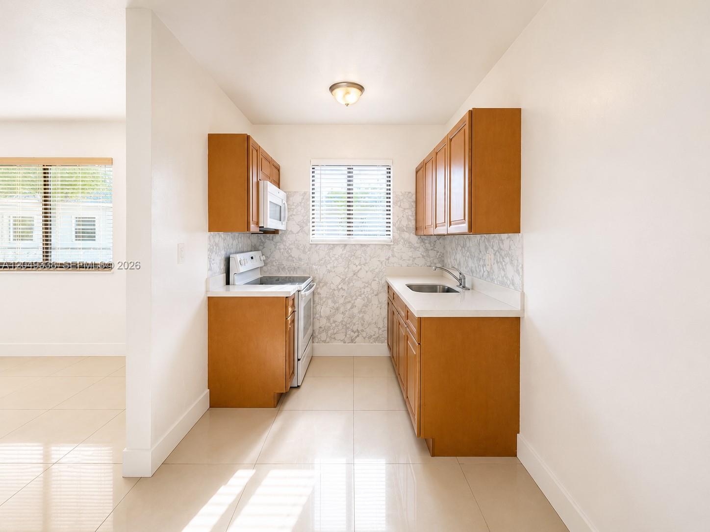 A galley kitchen features wood cabinets, white countertops, a marble-patterned backsplash, and tile flooring — 1910 NW 31st St # 2, Miami FL 33142, MIAMI, FL