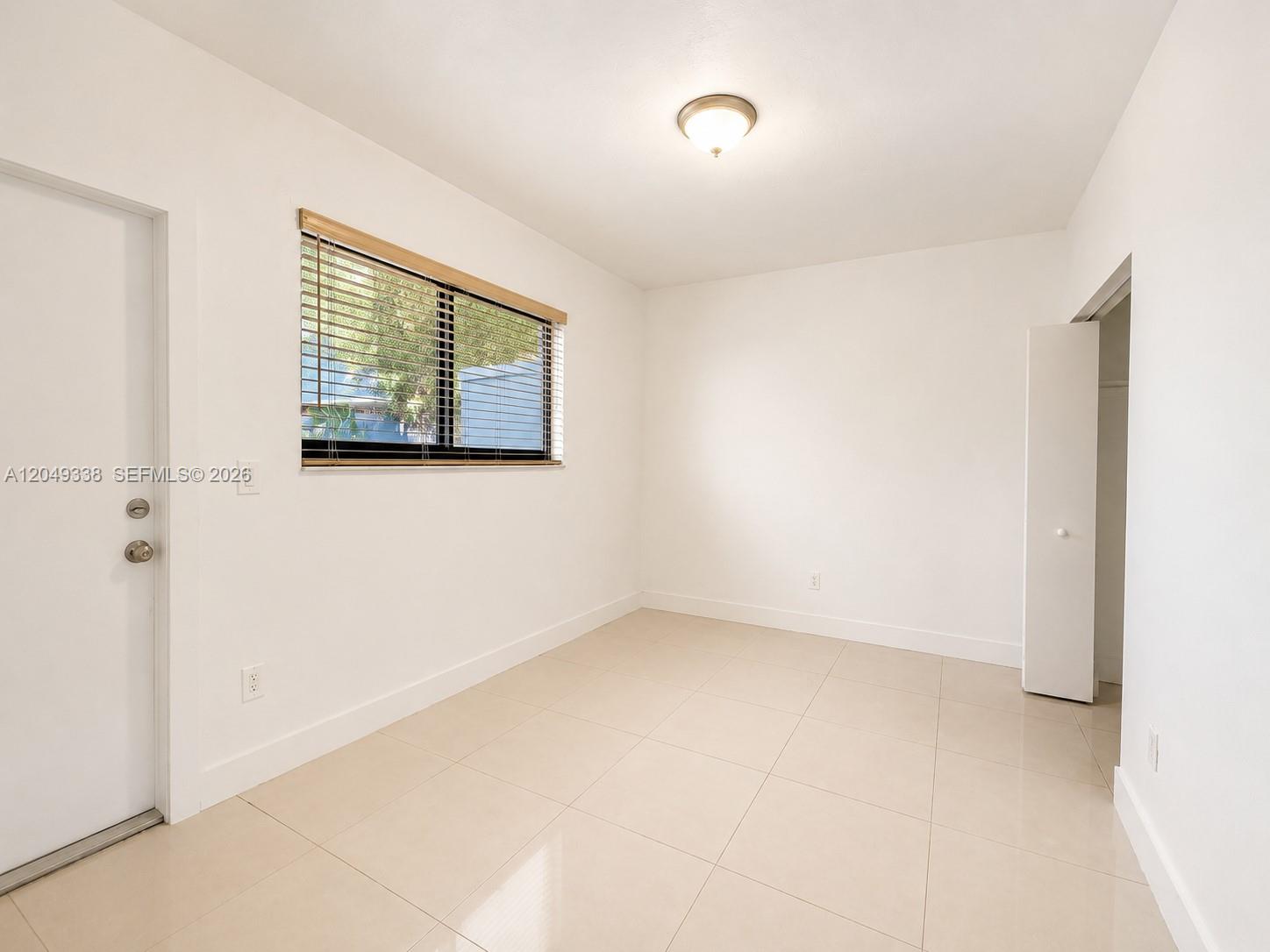 An empty room features white walls, light-colored tile flooring, a window with blinds, and a closet — 1910 NW 31st St # 2, Miami FL 33142, MIAMI, FL