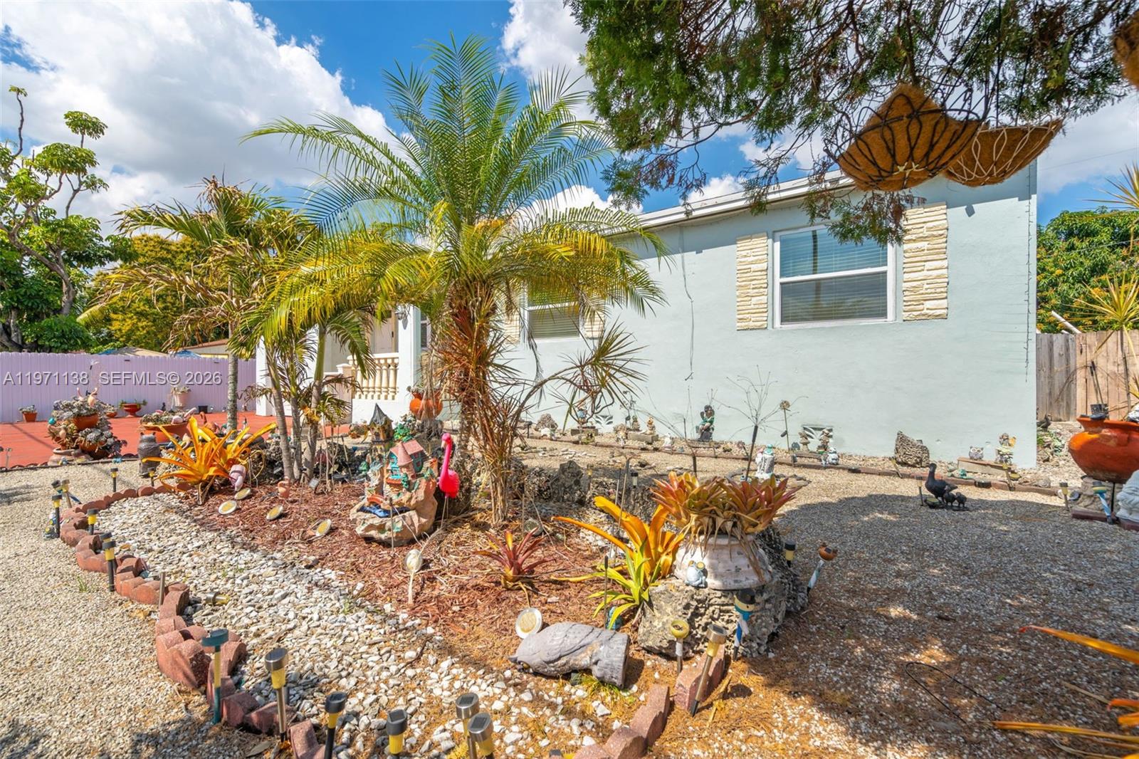 A light blue house exterior features a gravel yard with palm trees and decorative ornaments — 801 OPA LOCKA BLVD, Miami FL 33168, MIAMI, FL