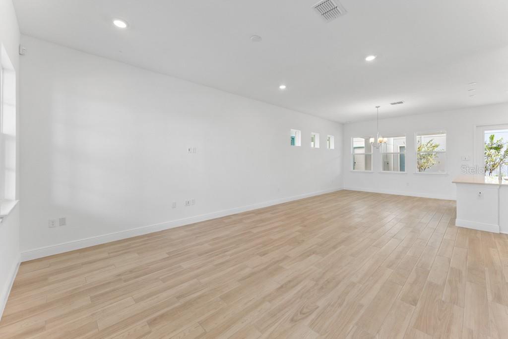 A bright, empty living room features white walls, recessed lighting, and light wood-look flooring — 10115 PEARSON AVENUE, ORLANDO, FL
