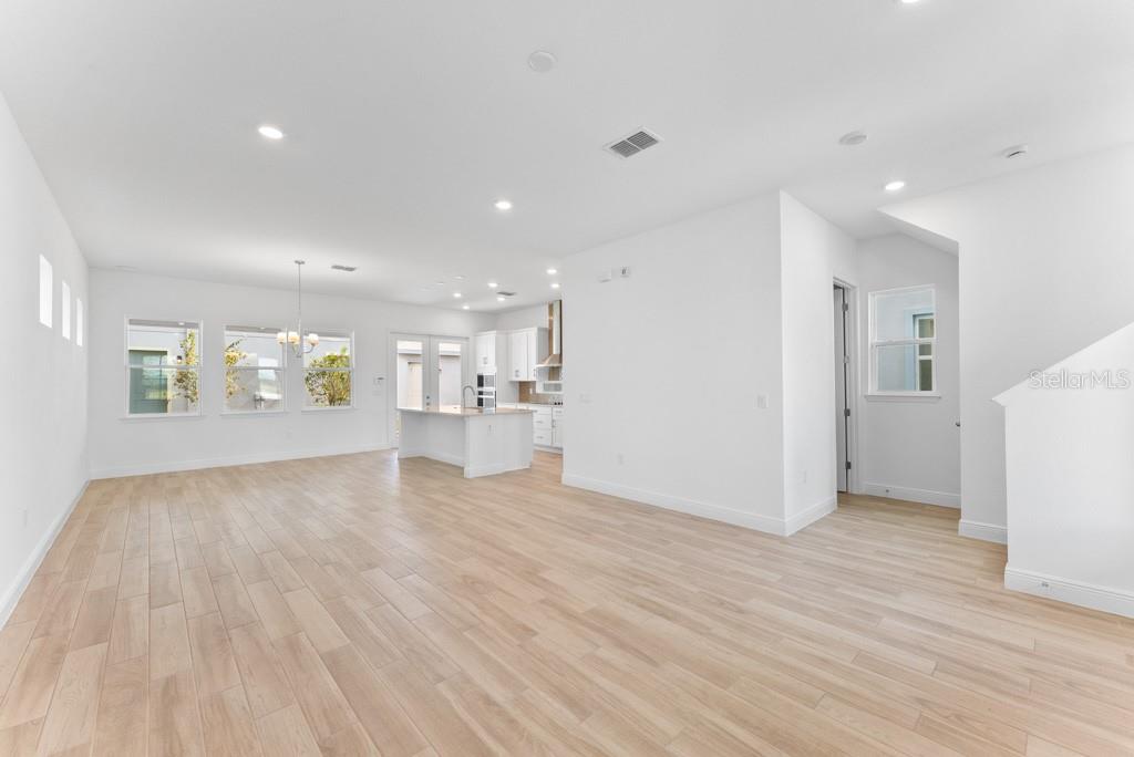An open-concept kitchen and living area with light wood-look flooring and white walls — 10115 PEARSON AVENUE, ORLANDO, FL
