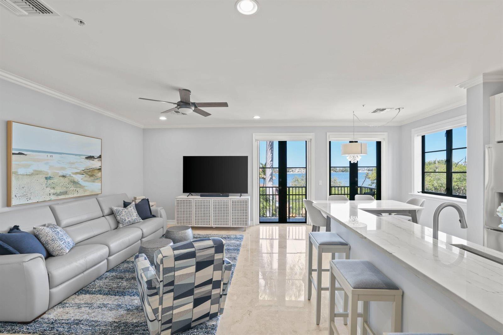 A bright living and dining area features white marble floors, a kitchen island, and balcony — 920 Via Villagio, Hypoluxo FL 33462, HYPOLUXO, FL