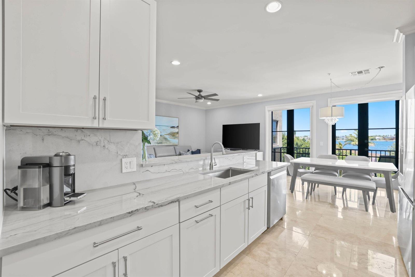 A modern white kitchen features marble countertops and overlooks a dining area with water views — 920 Via Villagio, Hypoluxo FL 33462, HYPOLUXO, FL