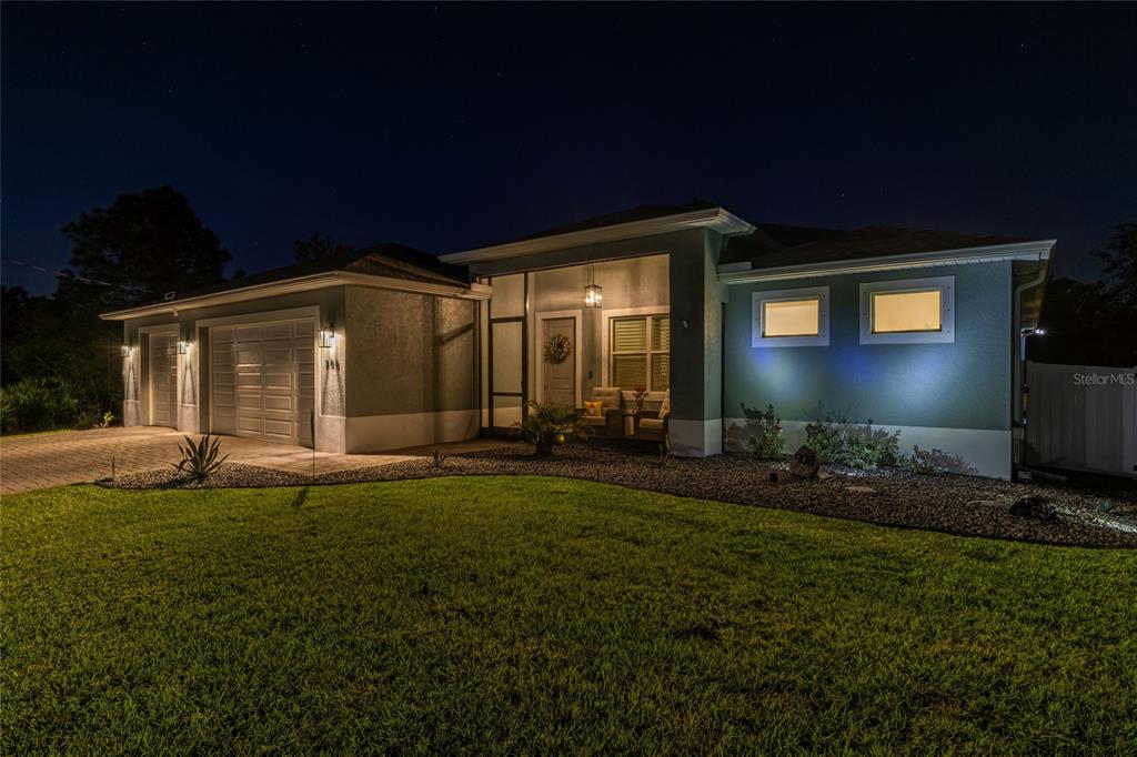 A single-story house exterior at night features a two-car garage and a screened front porch — 908 HIBISCUS AVENUE, LEHIGH ACRES, FL