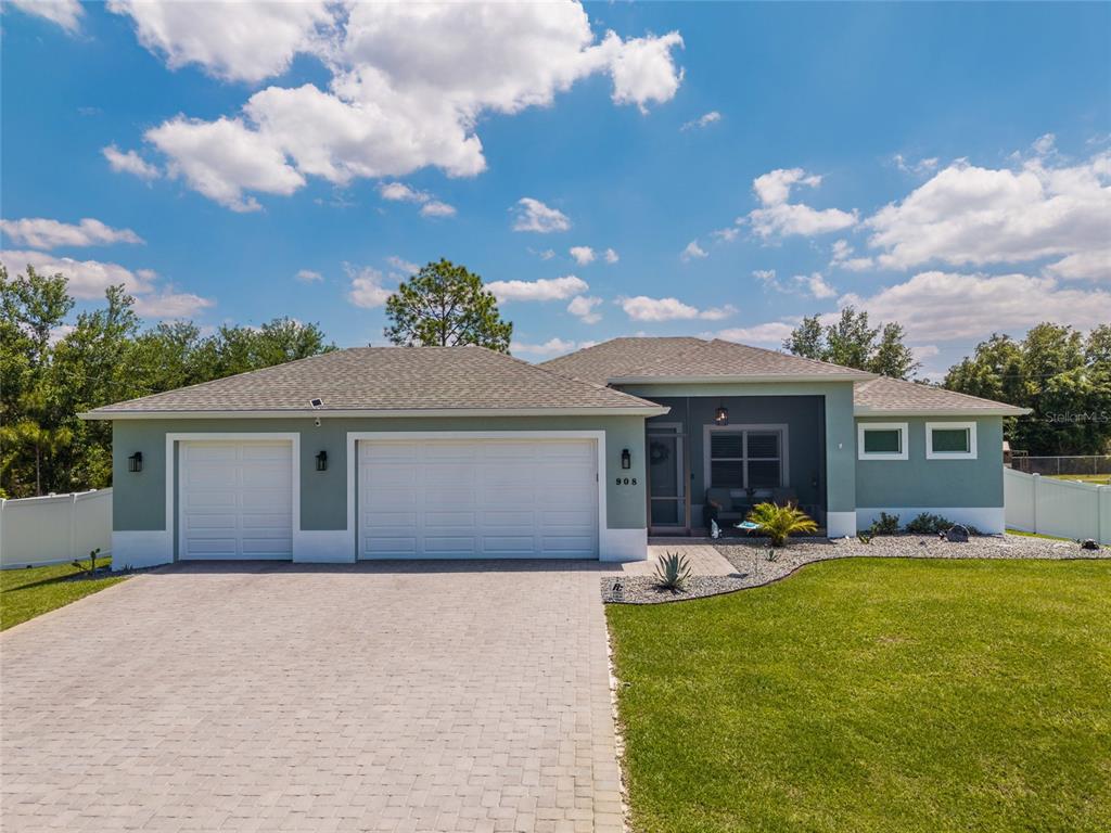 A single-story house with a three-car garage, light green siding, and a paved driveway — 908 HIBISCUS AVENUE, LEHIGH ACRES, FL