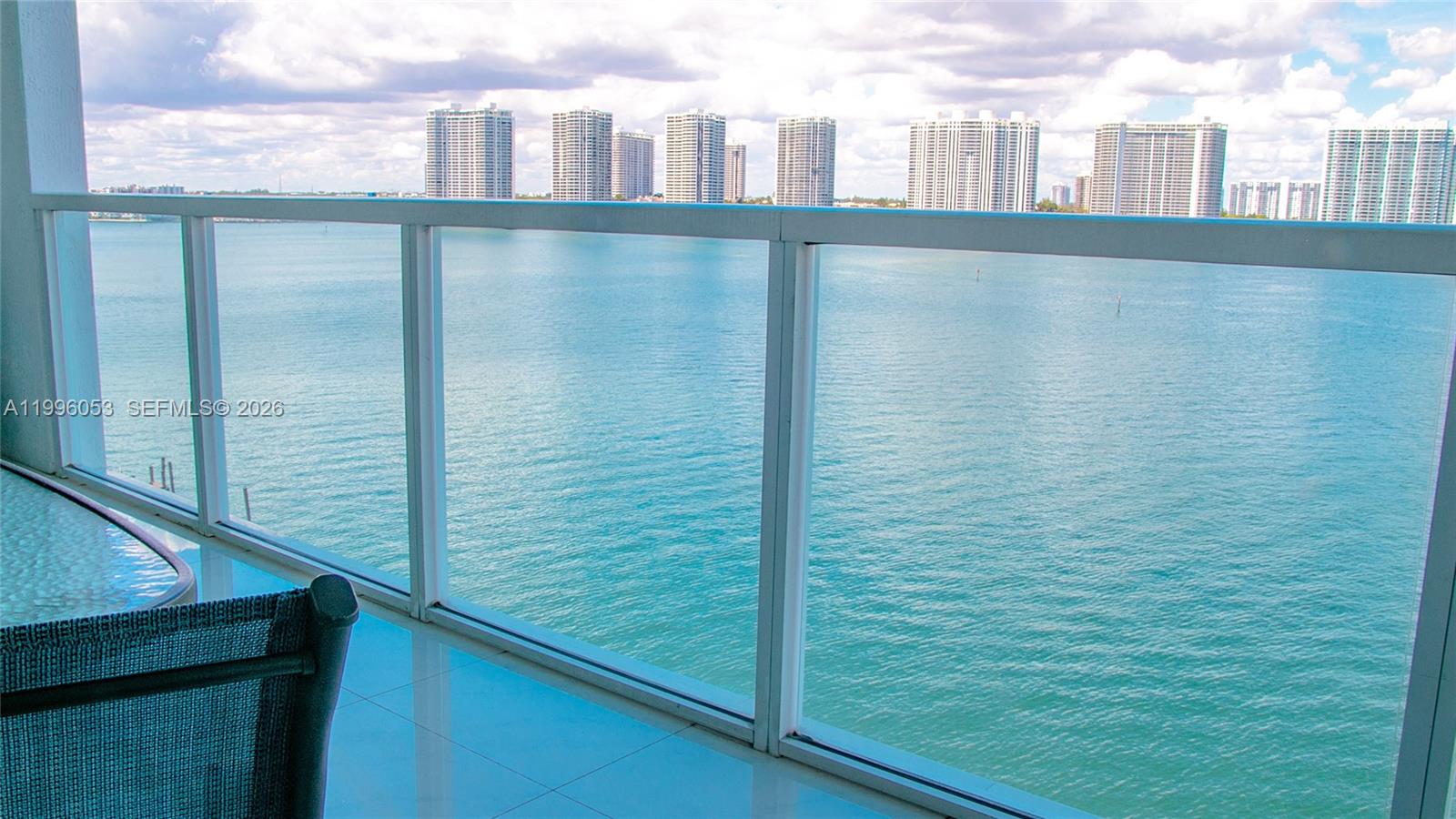 A balcony with a glass railing overlooks a body of water and distant high-rise buildings — SUNNY ISLES BEACH, FL