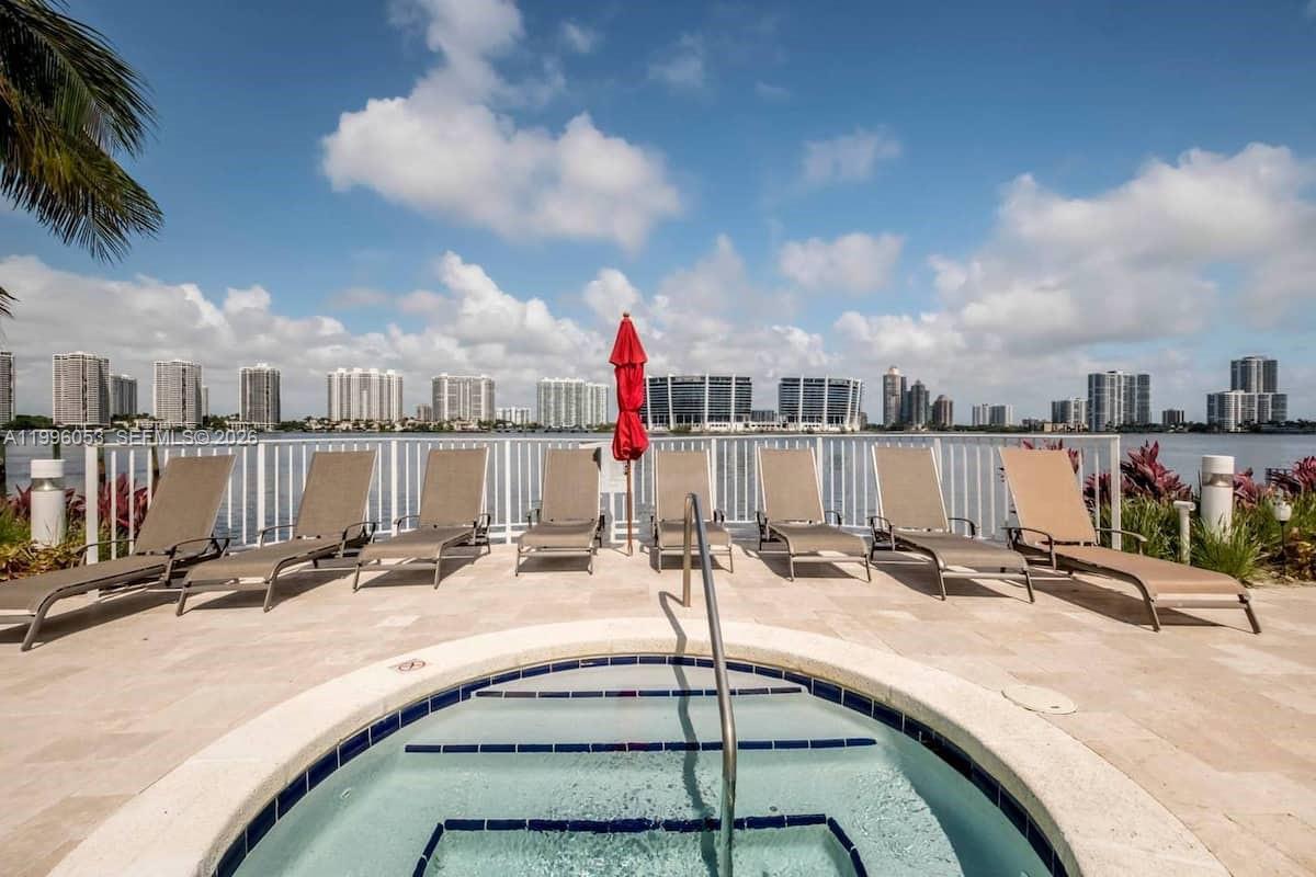 A hot tub sits on a patio with lounge chairs overlooking a bay and skyline — SUNNY ISLES BEACH, FL