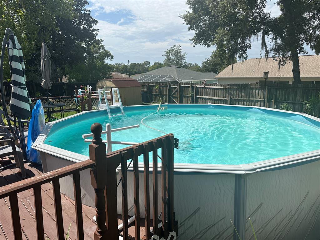 An above-ground swimming pool sits on a wooden deck in a fenced backyard — 2283 RENTON LANE, SPRING HILL, FL