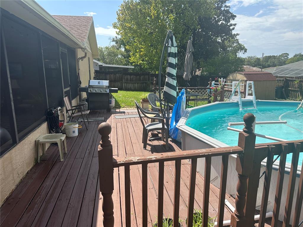 A wooden deck features an above-ground pool, a grill, patio furniture, and a screened porch — 2283 RENTON LANE, SPRING HILL, FL