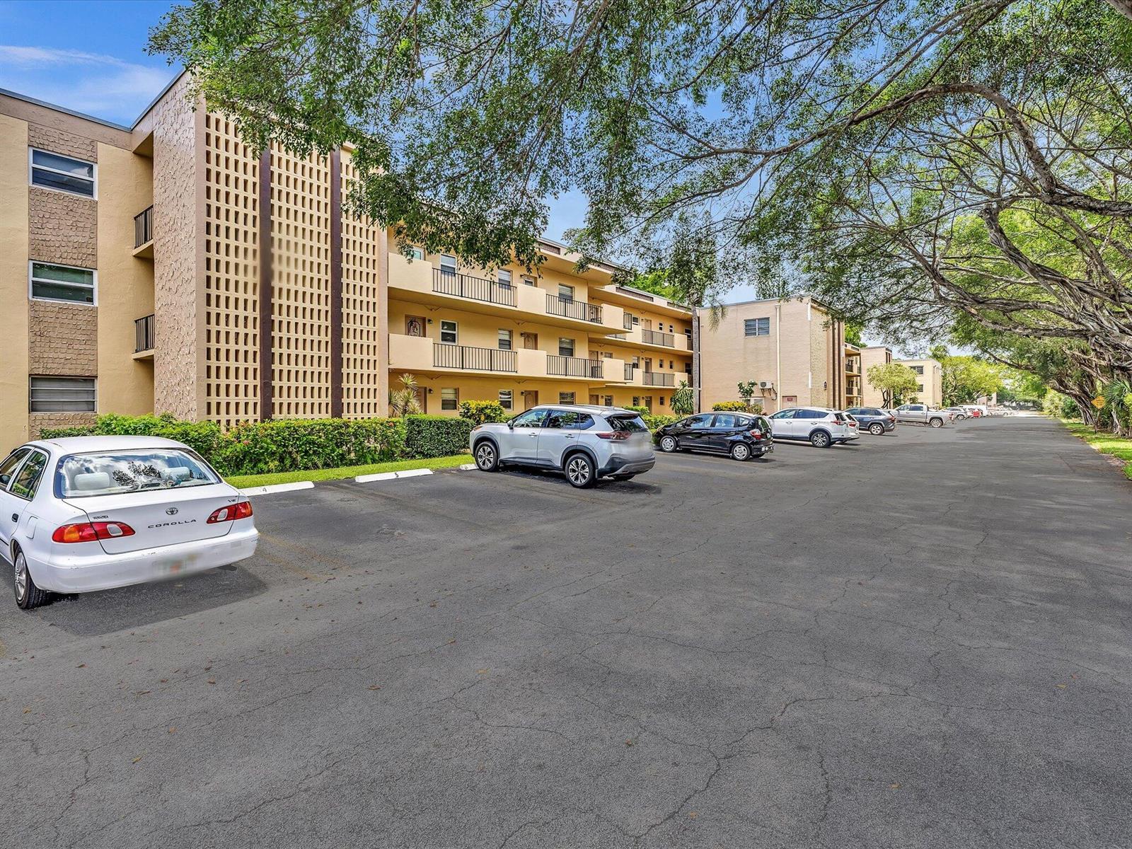 A multi-story apartment building with a parking lot in the foreground and large trees — 100 Ashbury Road # 103, Hollywood FL 33024, HOLLYWOOD, FL
